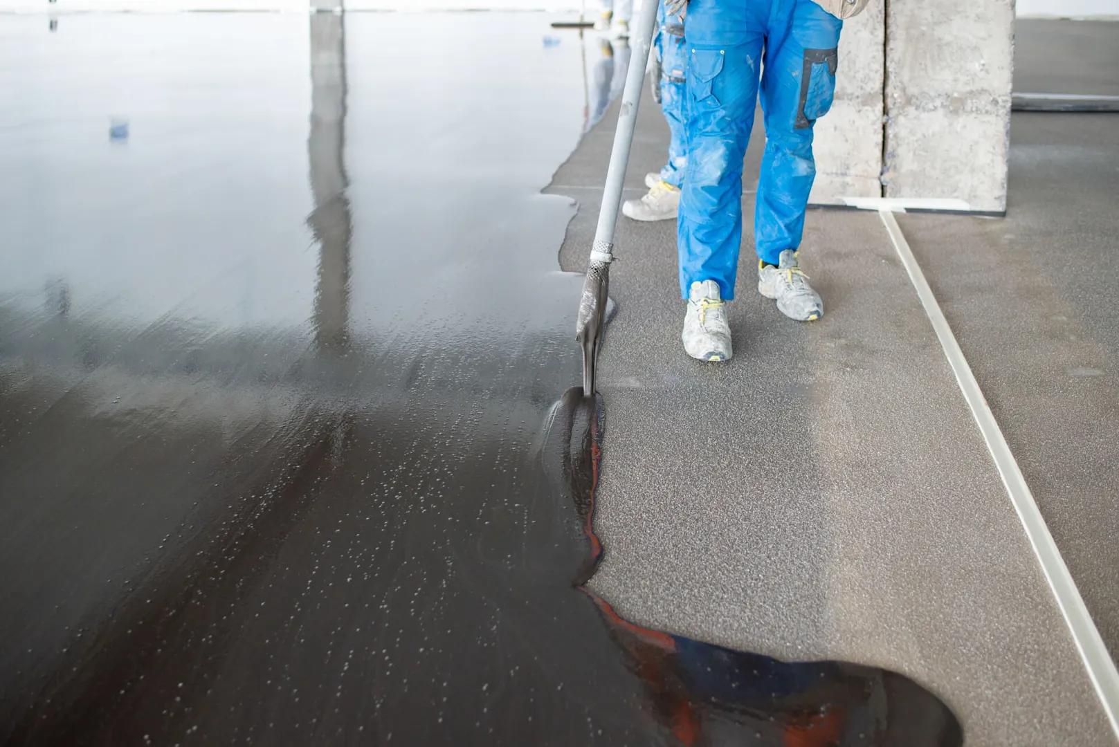 Worker applies black liquid coating on floor.
